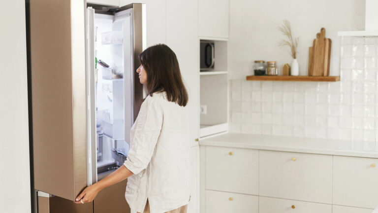 O botão mais ignorado da geladeira pode salvar seus alimentos 31 Stylish woman opening fridge and looking inside in new minimal white kitchen Housewife cleaning up